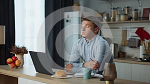 Exhausted businessman working laptop at kitchen table worried about work fail.