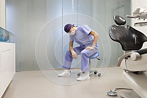 Exhausted dentist  sitting on dental saddle - price of success