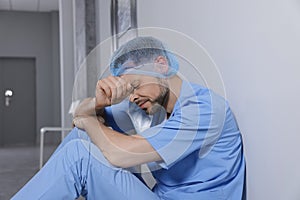 Exhausted doctor near grey wall in hospital corridor