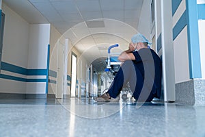 Exhausted doctor sitting on floor against in corridor at hospital