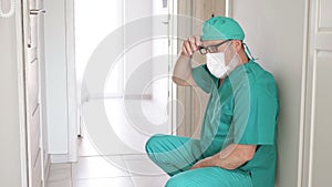 Exhausted elderly doctor sat down to rest on the floor in the hospital corridor.