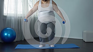 Exhausted fat man sitting on floor with dumbbells, tiring workout program, sport