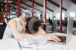 Exhausted fatigued young business woman sleeping on table at workplace