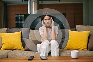 Exhausted frowning young woman suffer strong headache, migraine massaging temples sitting on sofa at home