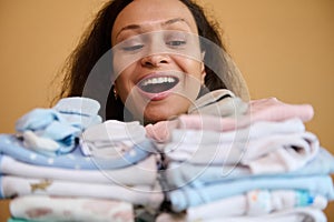 Exhausted but happy woman, smiling with a beautiful toothy smile, holding clean ironed baby clothes. Birth of a child