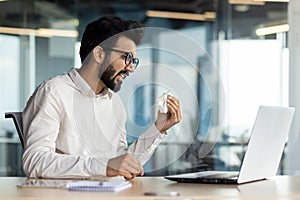 Exhausted indian businessman wiping sweat at office, overburdened with work on laptop