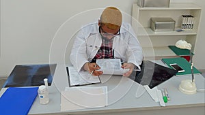 Exhausted male doctor falling alseep over medical papers at his desk
