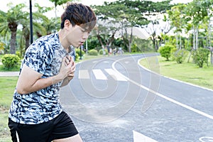 Exhausted male runner suffering painful angina pectoris or asthma breathing problems after running at the park. Sport and