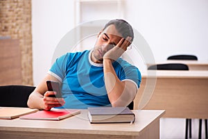 Exhausted male student preparing for the exams in the classroom