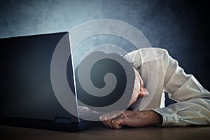 Exhausted man sleeps on laptop at office desk