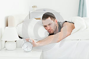 Exhausted man switching off his alarm clock