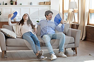 Exhausted man and woman waving paper fans, resting on couch