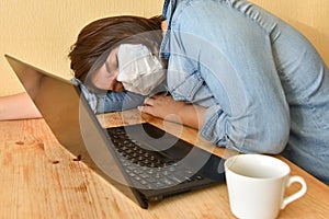 Exhausted masked woman fell asleep while working on laptop at home