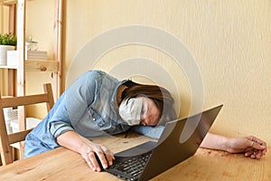 Exhausted masked woman fell asleep while working on laptop at home