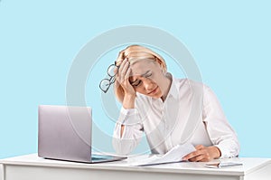 Exhausted mature business lady sitting at her desk with laptop and documents over blue studio background