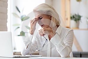 Exhausted mature employee suffer from migraine at workplace