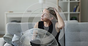 Exhausted mature homeowner woman getting cool, refresh at electric fan