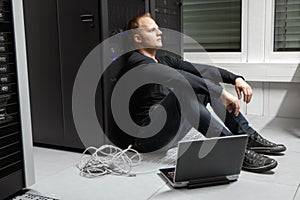 Exhausted Mid Adult Male Technician Against Server Rack At Datacenter