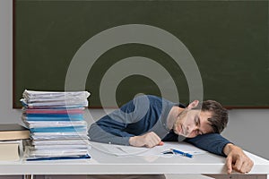 Exhausted and overworked teacher is sleeping on desk in classroom