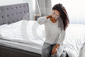 Portrait of black woman with neck pain sitting on bed