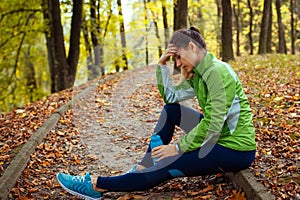 Exhausted runner having rest after workout in autumn park. Tired woman holding water bottle. Sportive lifestyle