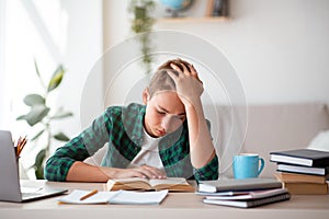Exhausted schooler sitting at desk in his room, studying