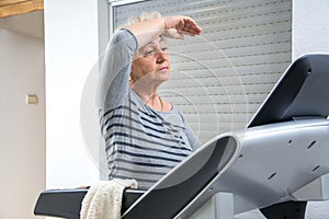 Exhausted senior woman on a treadmill at home. Active seniors, home quarantine and Corona virus Covid-19 concept