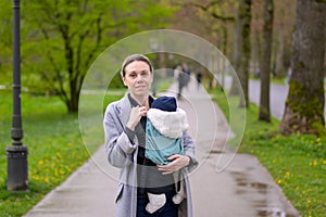 Exhausted and stressed late-term mother in her 40s holding her newborn baby in a baby carrier and looking annoyed to the camera