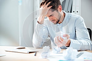 Exhausted stressed young man crumpling paper at workplace
