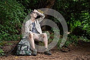 An exhausted and sweaty Asian male hiker sits on a stone, resting and taking a break