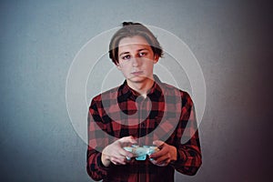 Exhausted teenage guy playing video games  on grey wall background. Sleepy and tired boy holding joystick console,