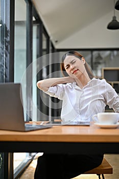 Exhausted, tired and overworked Asian businesswoman at her desk suffering from neck pain