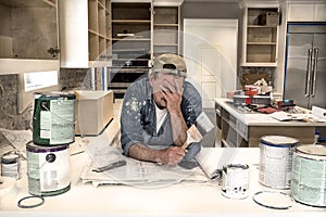 Exhausted, tired painter, face in hands holding wet paintbrush in messy home kitchen fixer upper remodel dripping paint cans photo