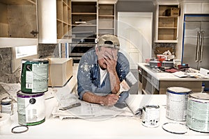 Exhausted and tired painter with face in hands holding wet paint brush in messy home kitchen with paint cans everywhere photo