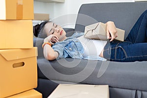 Exhausted, Tired Young Asian woman working overnight and sleep at couch with packing box feels exhaustion having day nap lack of