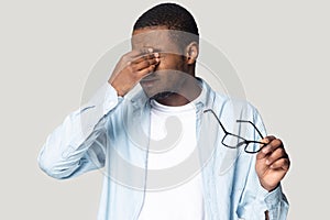 Exhausted unhealthy young african american man rubbing irritated eyes.