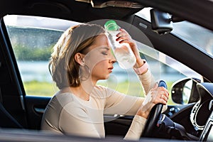 Exhausted woman driver feeling headache, sitting inside her car, applies a bottle of water to his forehead, hot weather