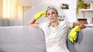 Exhausted woman in gloves sitting on sofa, cleaning service for tired housewives