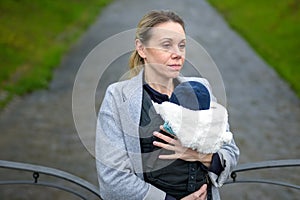 Exhausted woman holding and carrying her baby in a baby carrier