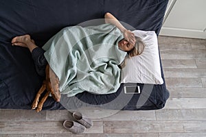 Exhausted woman lying in bed with dog at home suffering from strong tension headache, migraine, flu.