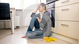 Exhausted woman sitting on floor at kitchen after cleaning house