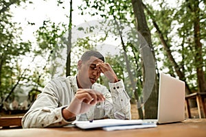 Exhausted young african american man sitting beside laptop