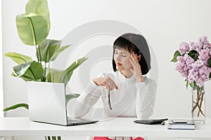 Exhausted young businesswoman sits at office desk take off glasses feel unwell massages temples, suffers from headache