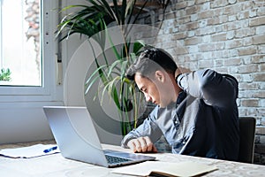 Exhausted young Caucasian male worker sit at desk massage neck suffer from strain spasm muscles. Tired unwell man overwhelmed with