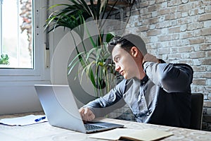 Exhausted young Caucasian male worker sit at desk massage neck suffer from strain spasm muscles. Tired unwell man overwhelmed with