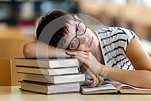 Exhausted young female studying and preparing for exam in college library. Education people concept