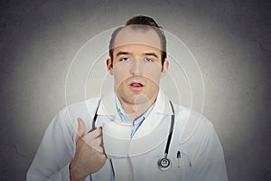 Exhausted young funny doctor holding cup coffee falling asleep