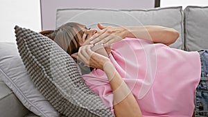 Exhausted young hispanic woman, speaking on the phone from her sofa, stifling a yawn, sporting short hair, lost in her living room