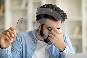 Exhausted Young Indian Man Taking Off Glasses, Feeling Eyes Fatigue After Work