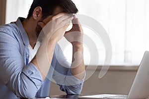 Exhausted young male employee sitting at workplace tired from work